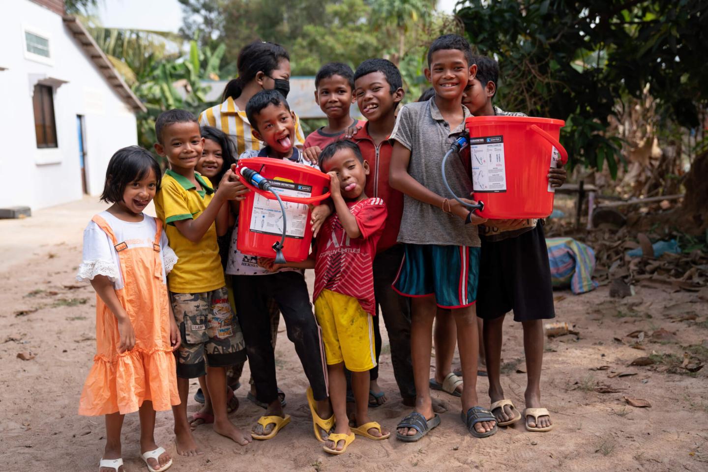 A group of kids in Cambodia pose for a photo holding water buckets
