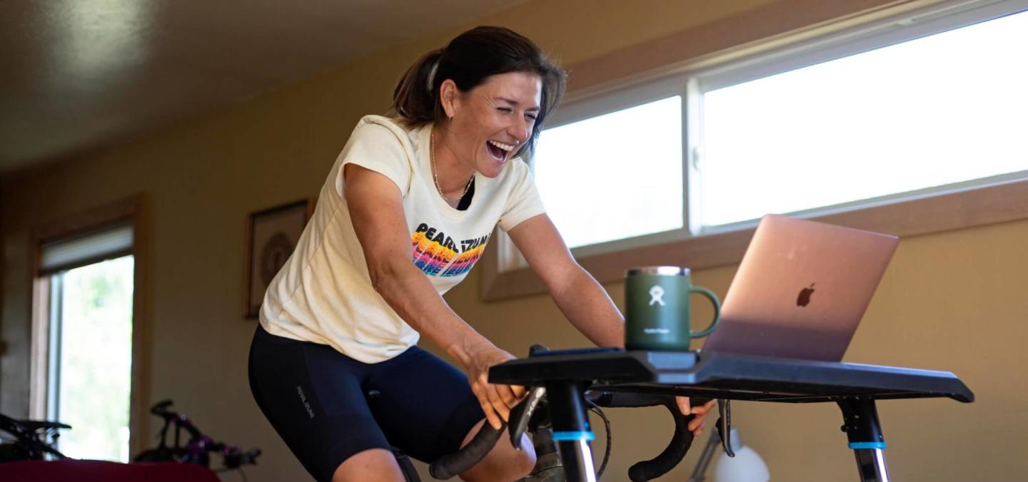 A person using an indoor bike while smiling at a laptop