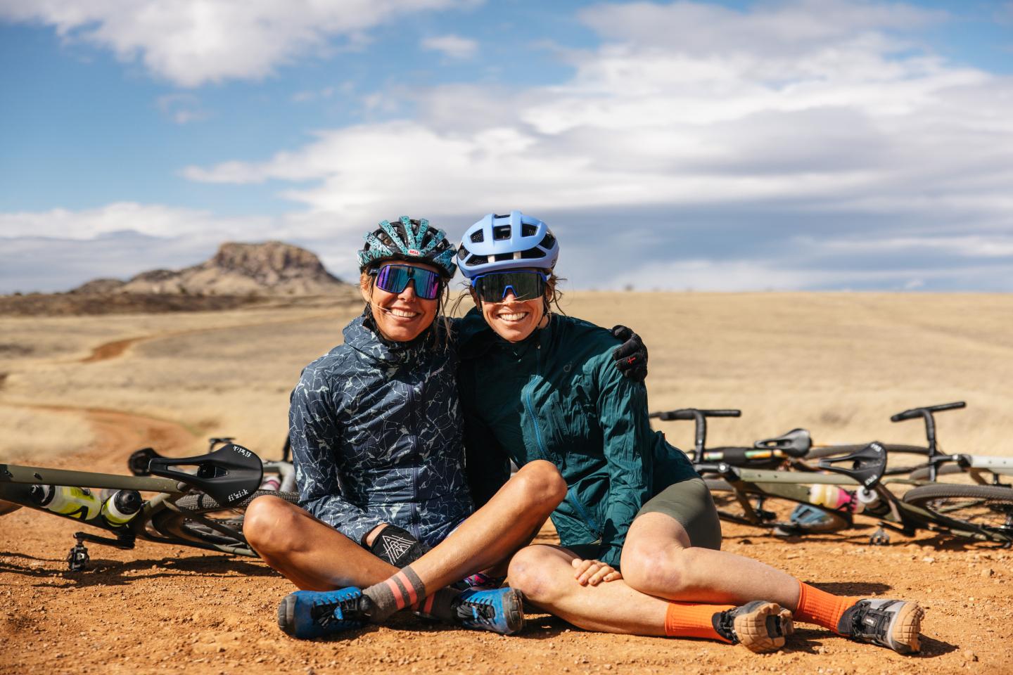 Two female cyclists seated in the desert smiling for the camera