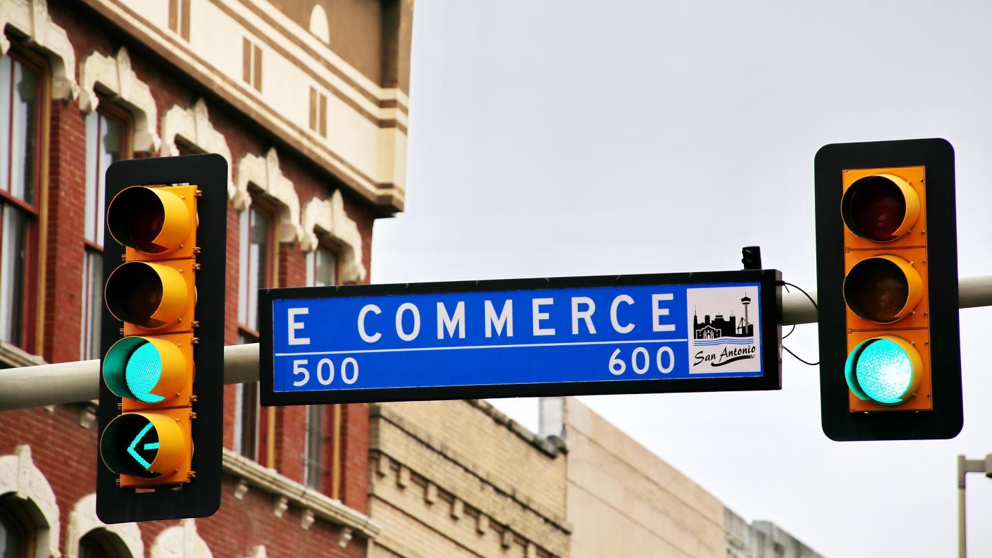 'E COMMERCE' on a street sign with traffic lights either side