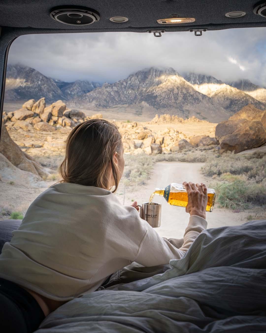 a woman pouring TINCUP whiskey in the back of a van with a mountain view