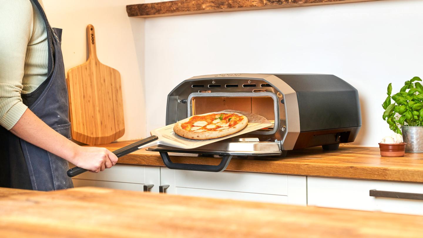 person cooking pizza in Ooni oven indoors