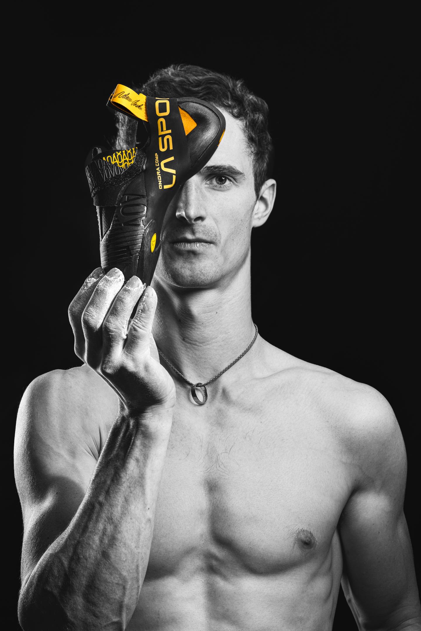 Adam Ondra holds a black and yellow Ondra Comp climbing shoe