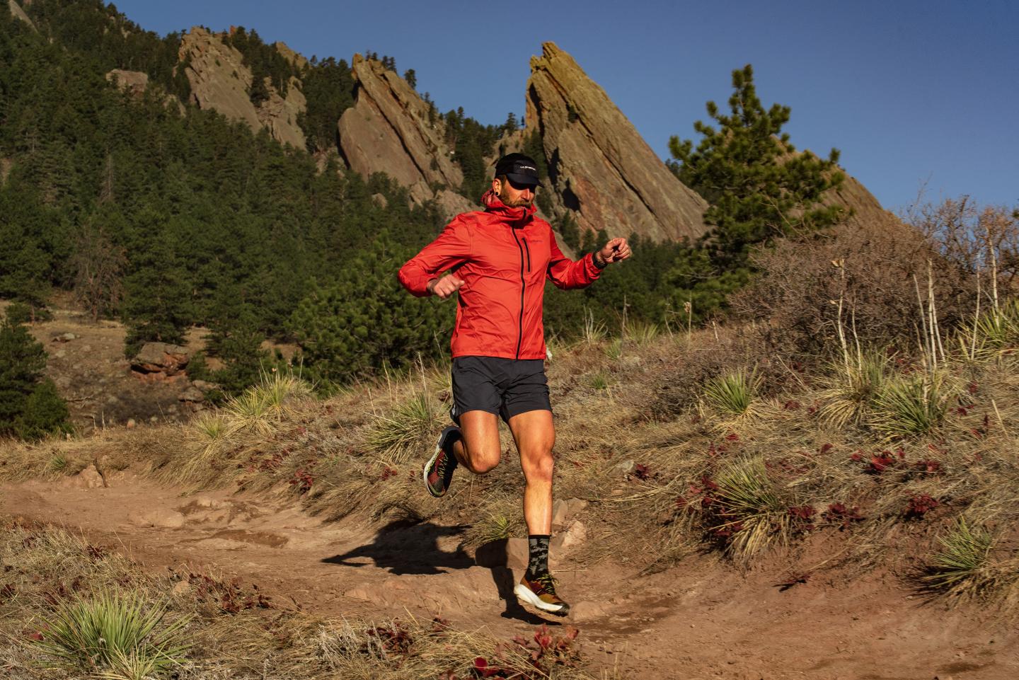 Trail runner in red jacket on a sunny day, mountains in the background.