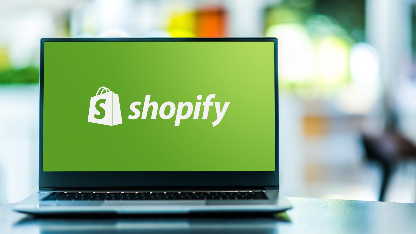 Laptop displaying Shopify logo, green background, blurred office setting