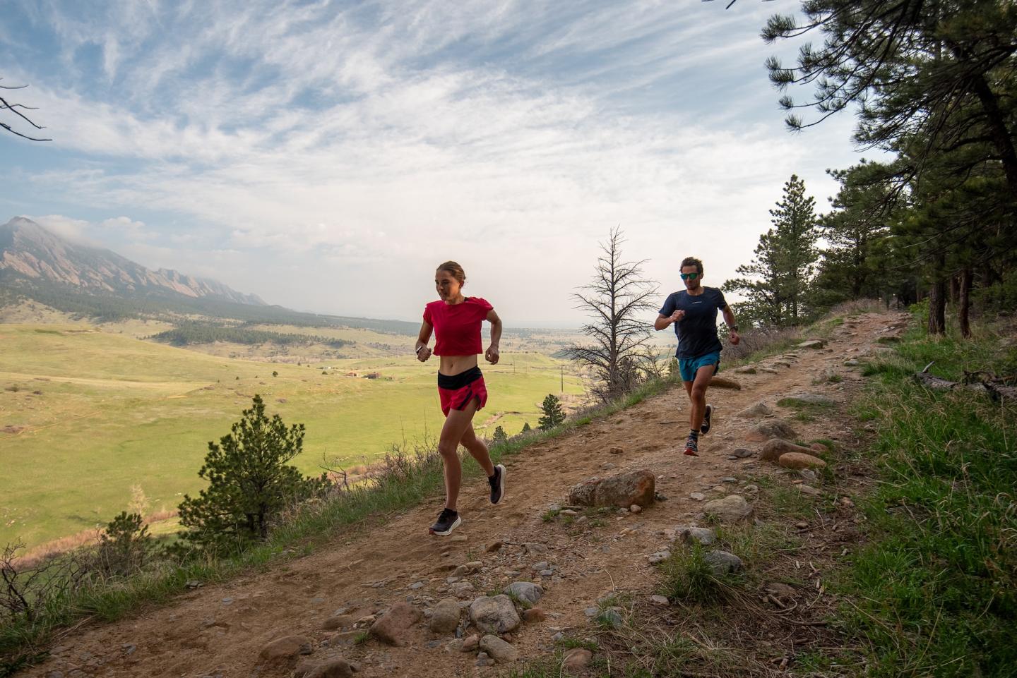 Trail runners on a dirt path with a scenic mountain backdrop.