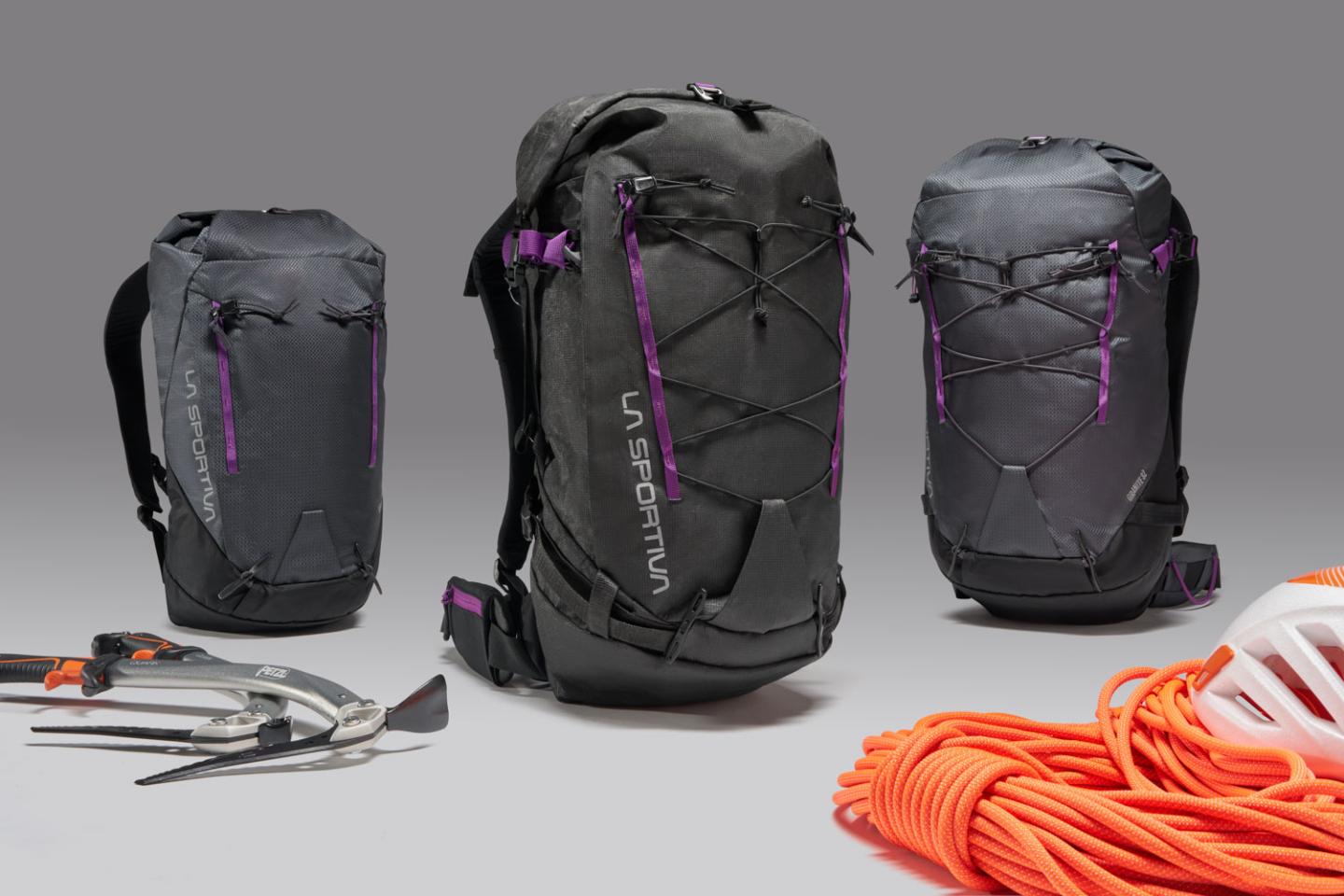 Three black backpacks with orange climbing gear and tools on a gray background.