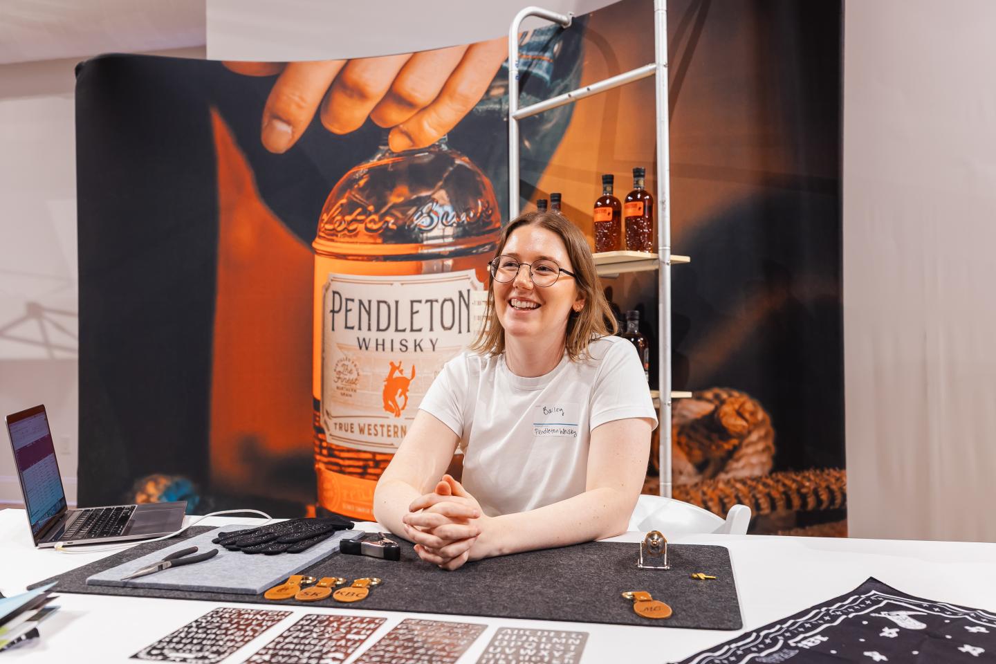 Smiling woman at a booth with Pendleton whiskey display in background.