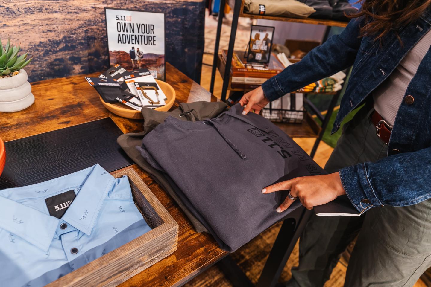 Clothing display on wooden table with folded pants and blue shirt.