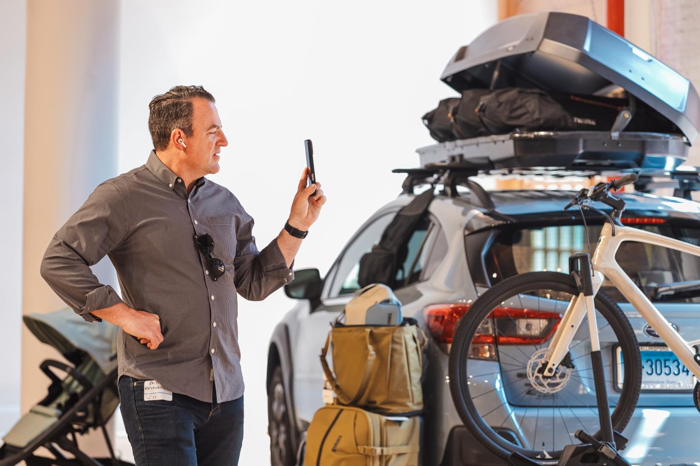 Man photographing packed car with bike on rear in brightly lit room.