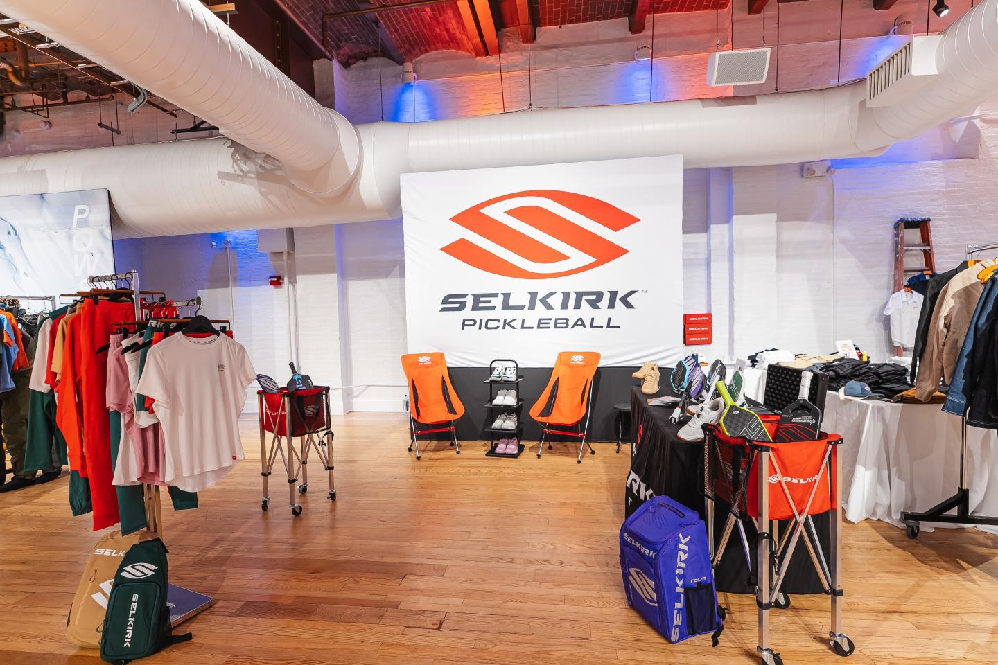 Selkirk Pickleball store with clothing racks and carts in a wood-floored room.