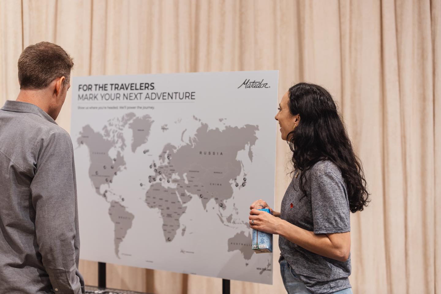 Two people discuss a world map on a stand.