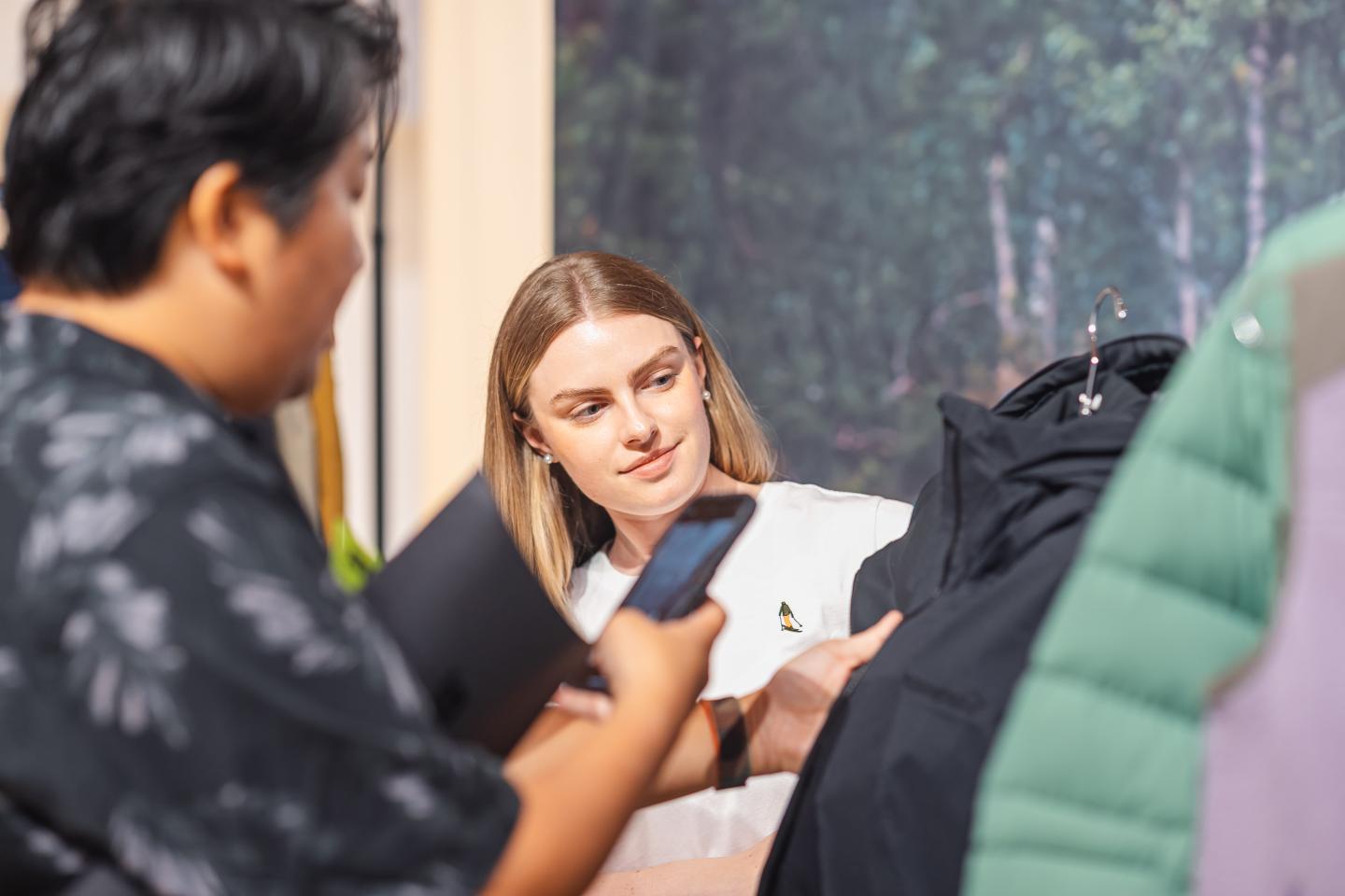 Two people examining a jacket on a hanger indoors.