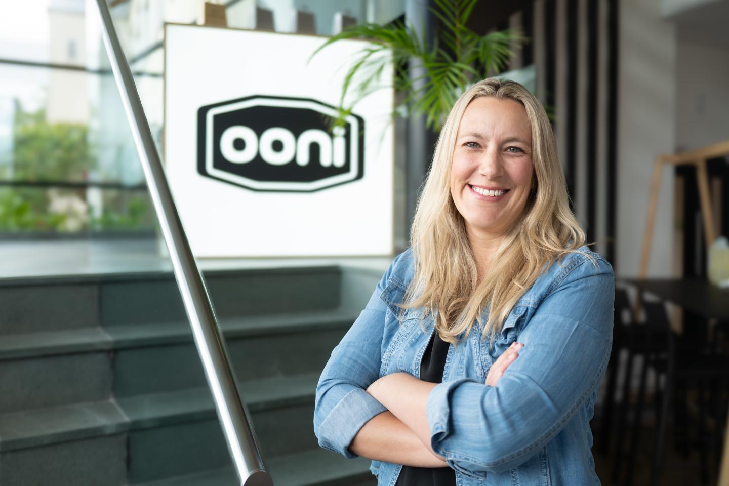 Smiling woman with crossed arms in front of "Ooni" sign.