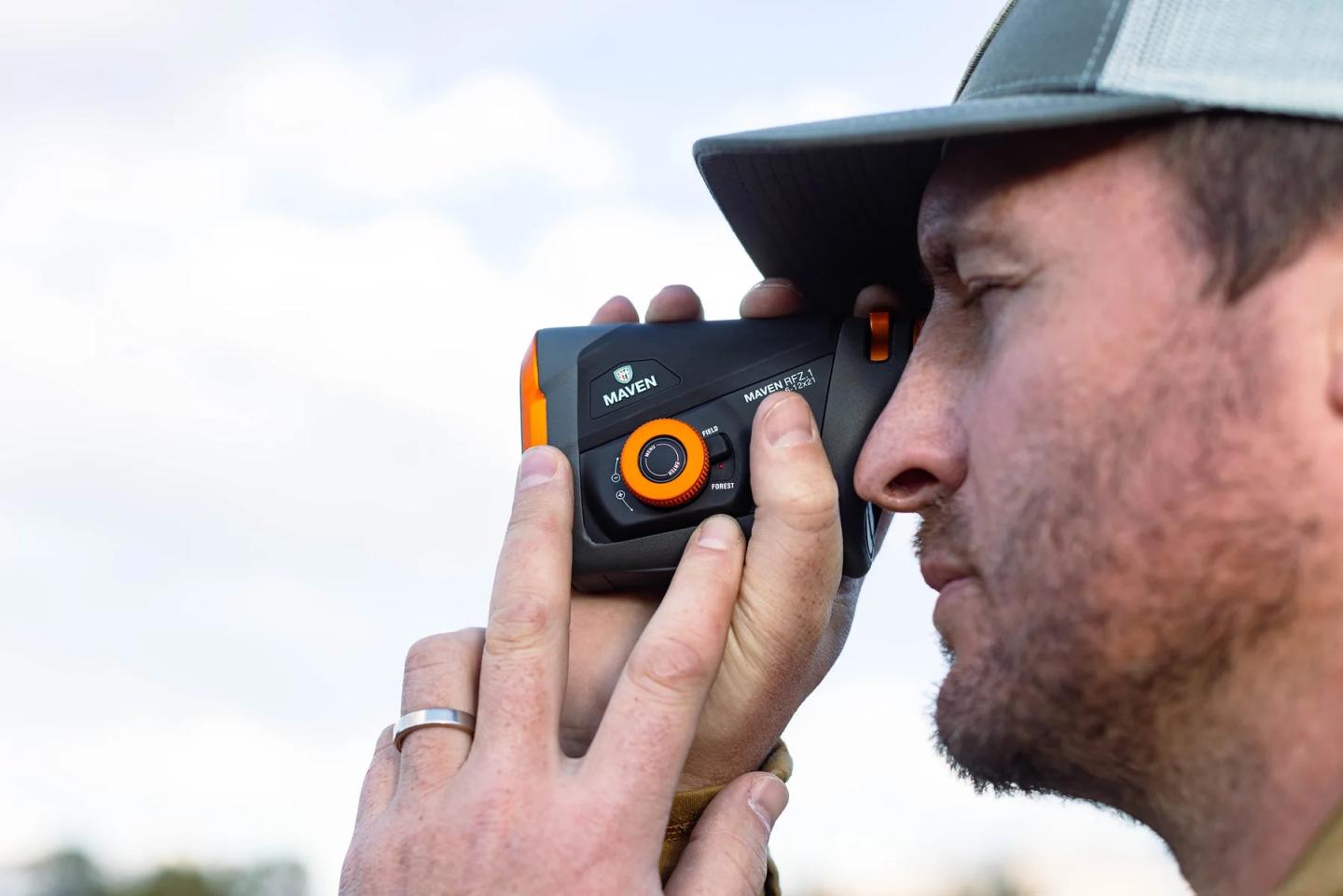 Man using a rangefinder outdoors, wearing a cap.