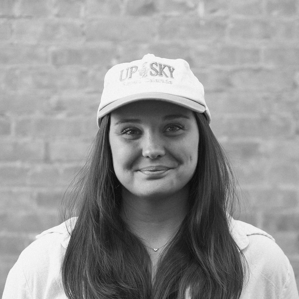 Black and white photo of a smiling person in a cap against a brick wall.
