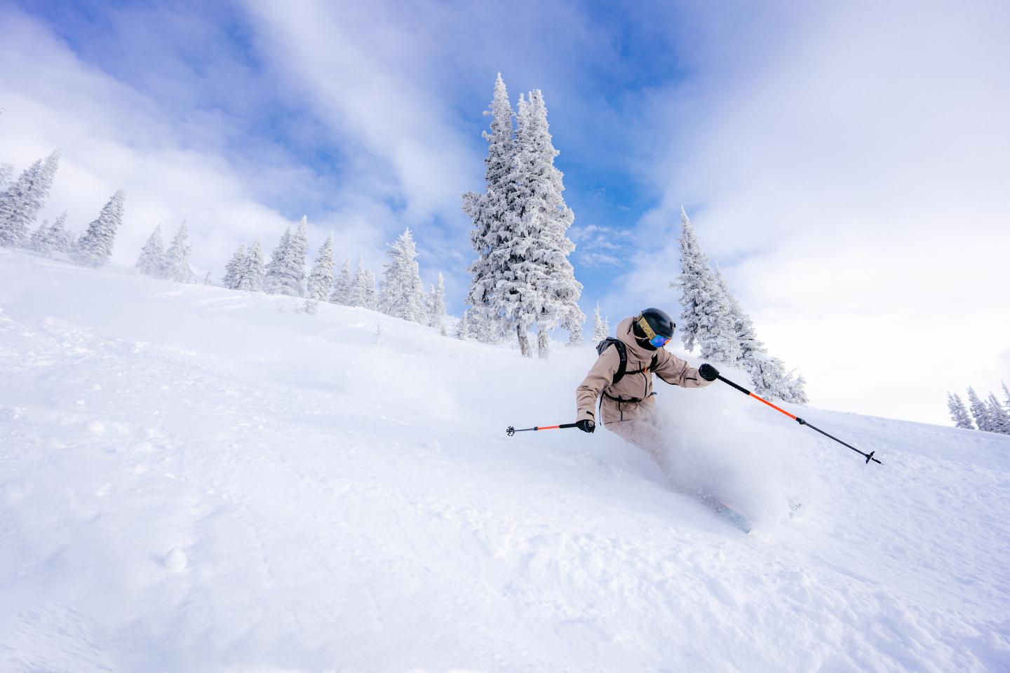 Skier in action on snowy slope with trees, under a clear blue sky.