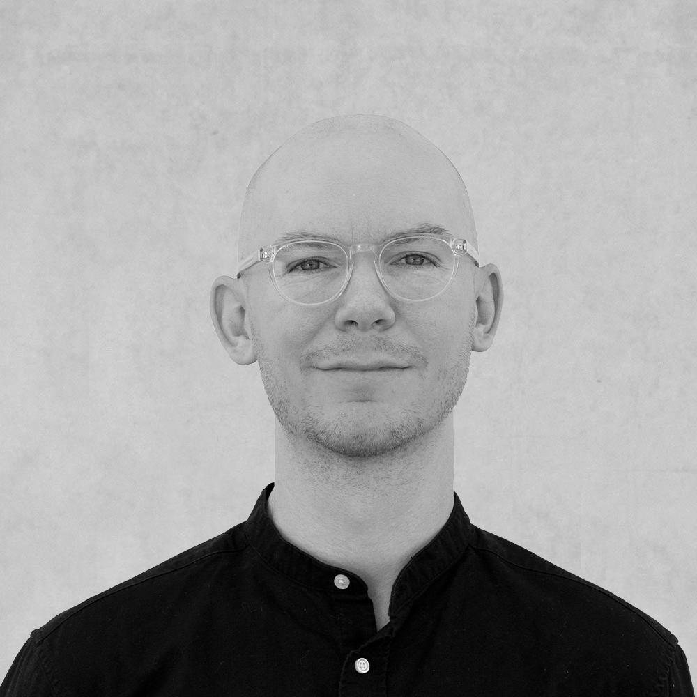 person wearing glasses, smiling slightly against a neutral background.