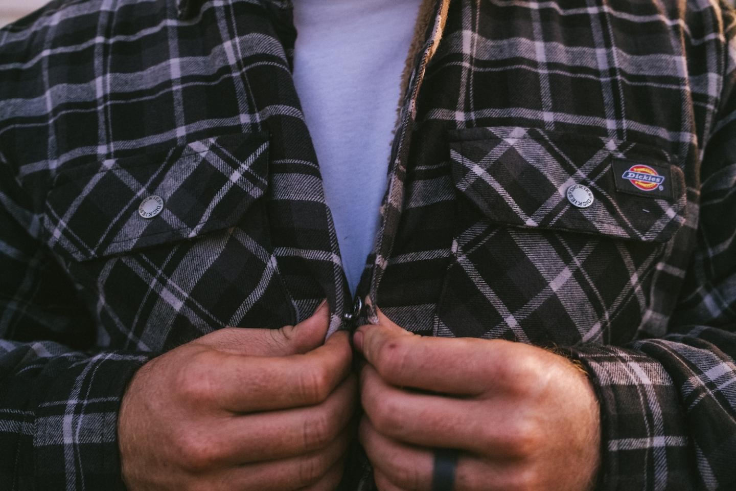 Plaid shirt being buttoned by a person with tattooed fingers.