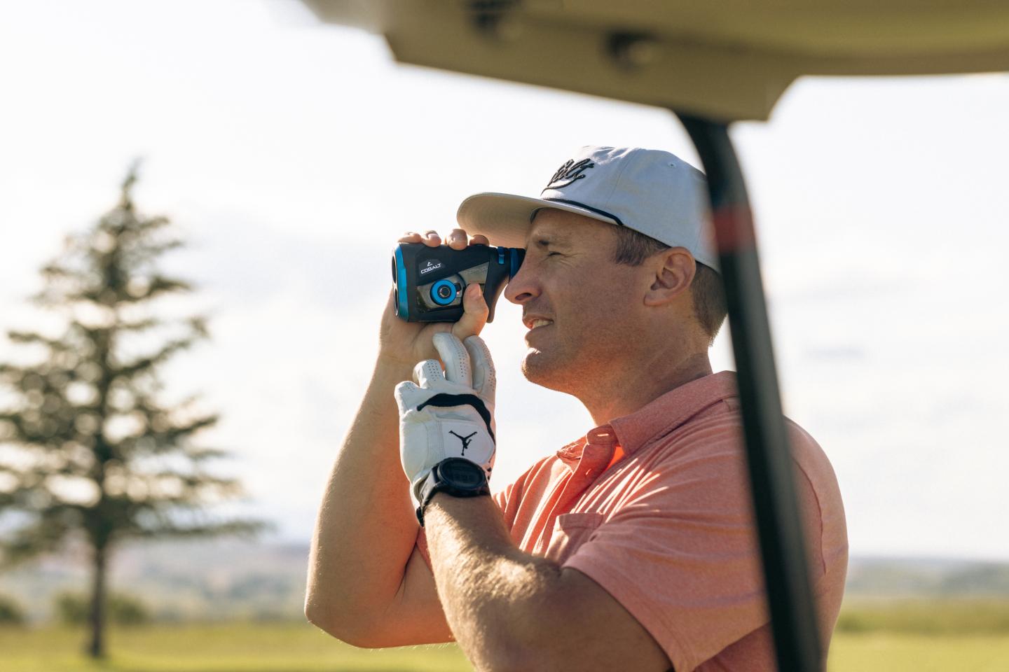Man in golf attire using a Cobalt rangefinder on course, sunny day.