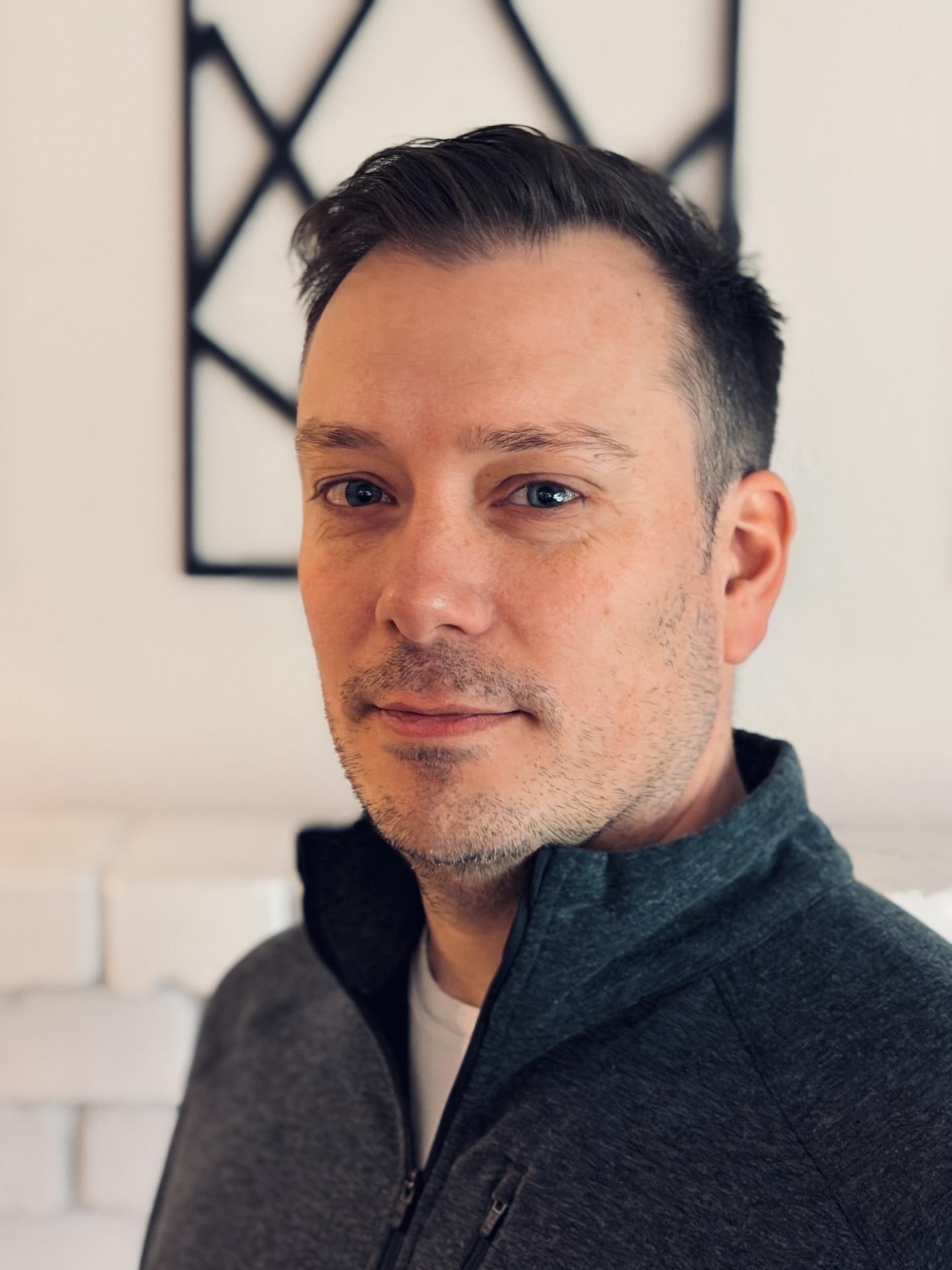 Man in a gray sweater with short hair and a neutral expression.