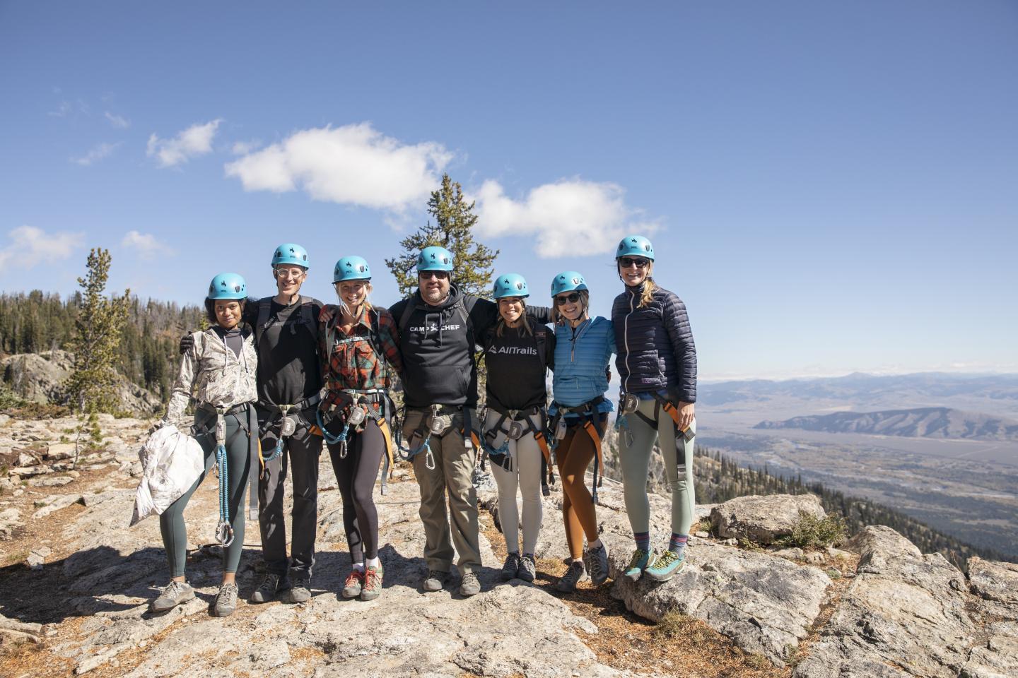 Group of hikers with helmets on a rocky mountain peak under clear sky.