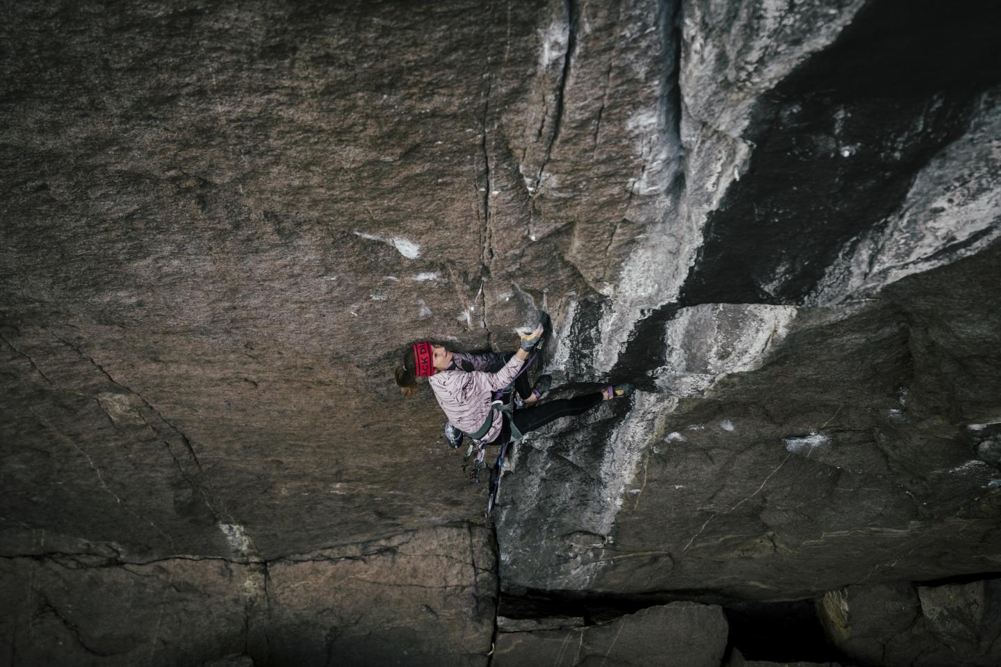 Rock climber ascending a steep, dark cliff face.