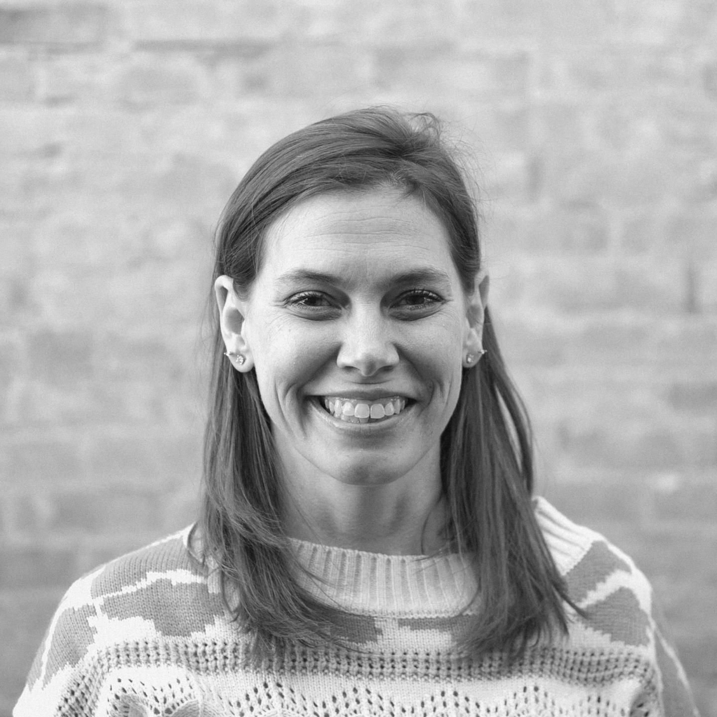 Smiling woman in a sweater, black and white photo, brick wall background.