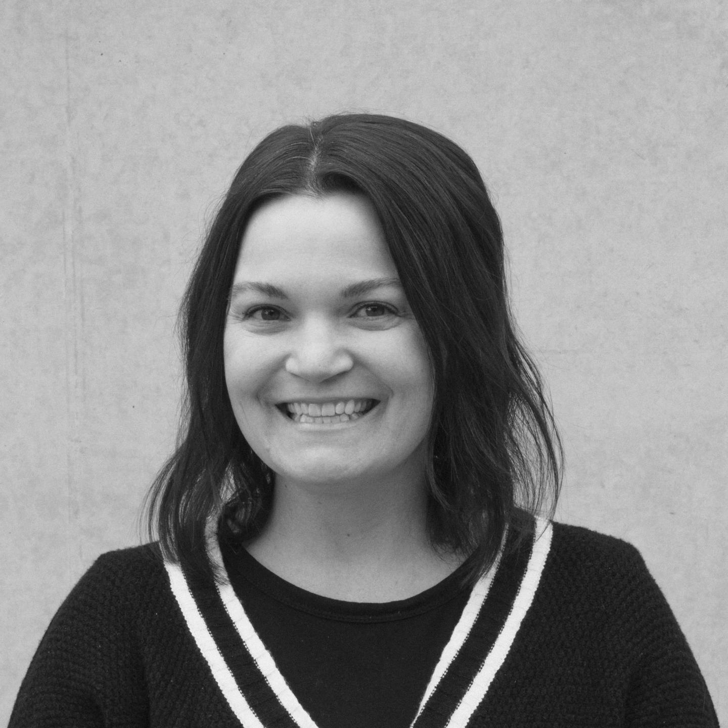Smiling person with shoulder-length hair against a plain background.