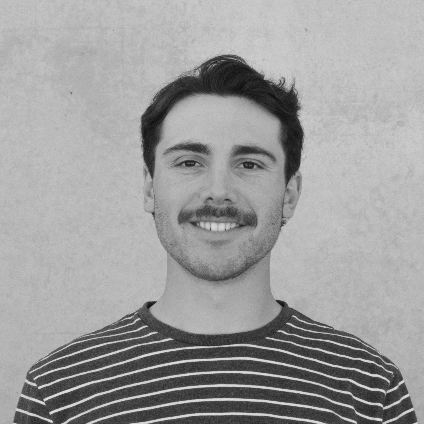 Smiling man with a striped shirt against a plain background.