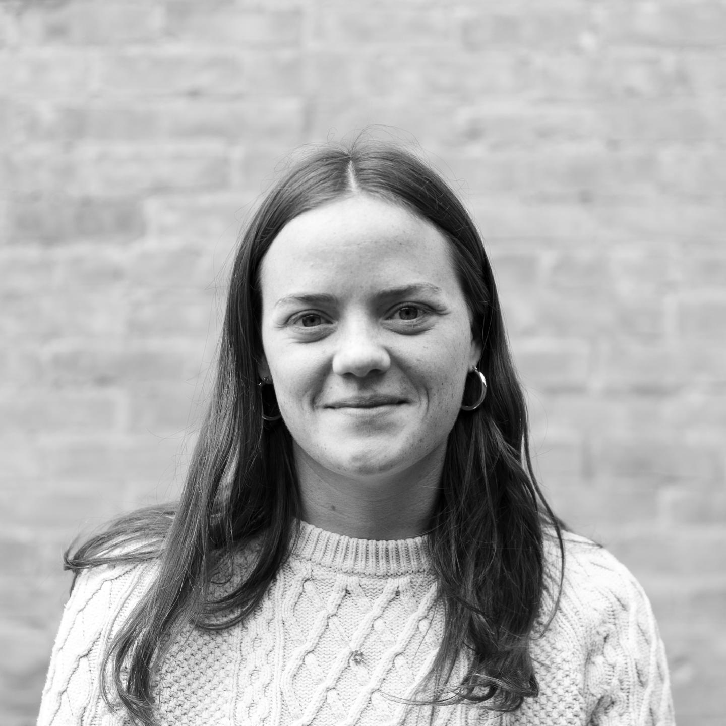 Black and white photo of a person smiling, standing against a brick wall.