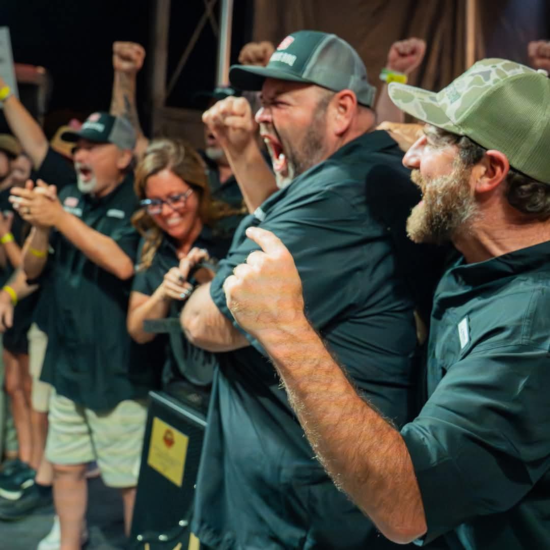 Excited group celebrating, fists raised, wearing matching dark attire.