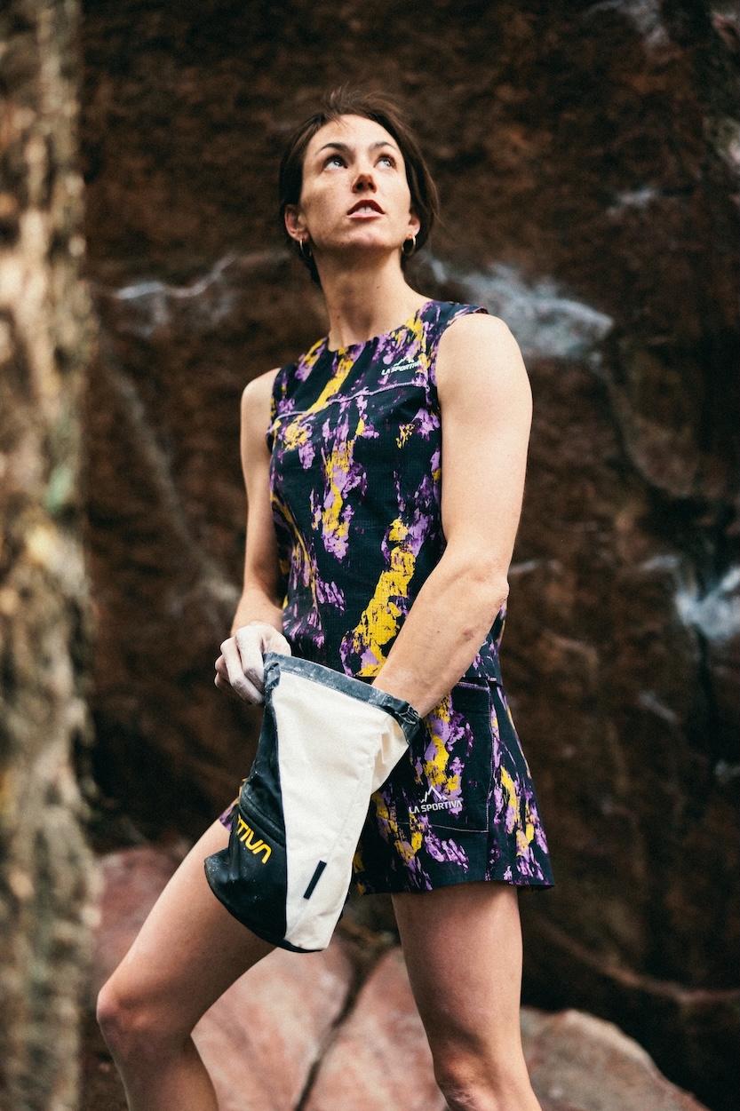 Climber with chalk bag gazes upwards on a rocky background.