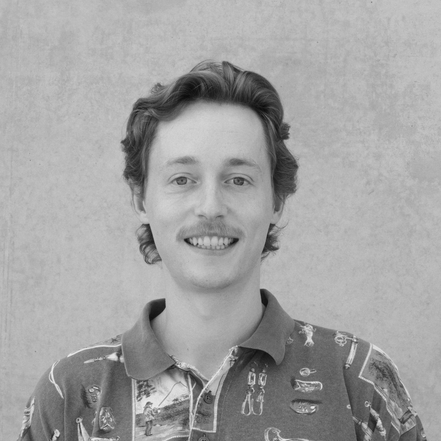 Smiling person with curly hair in a patterned shirt, gray textured background.