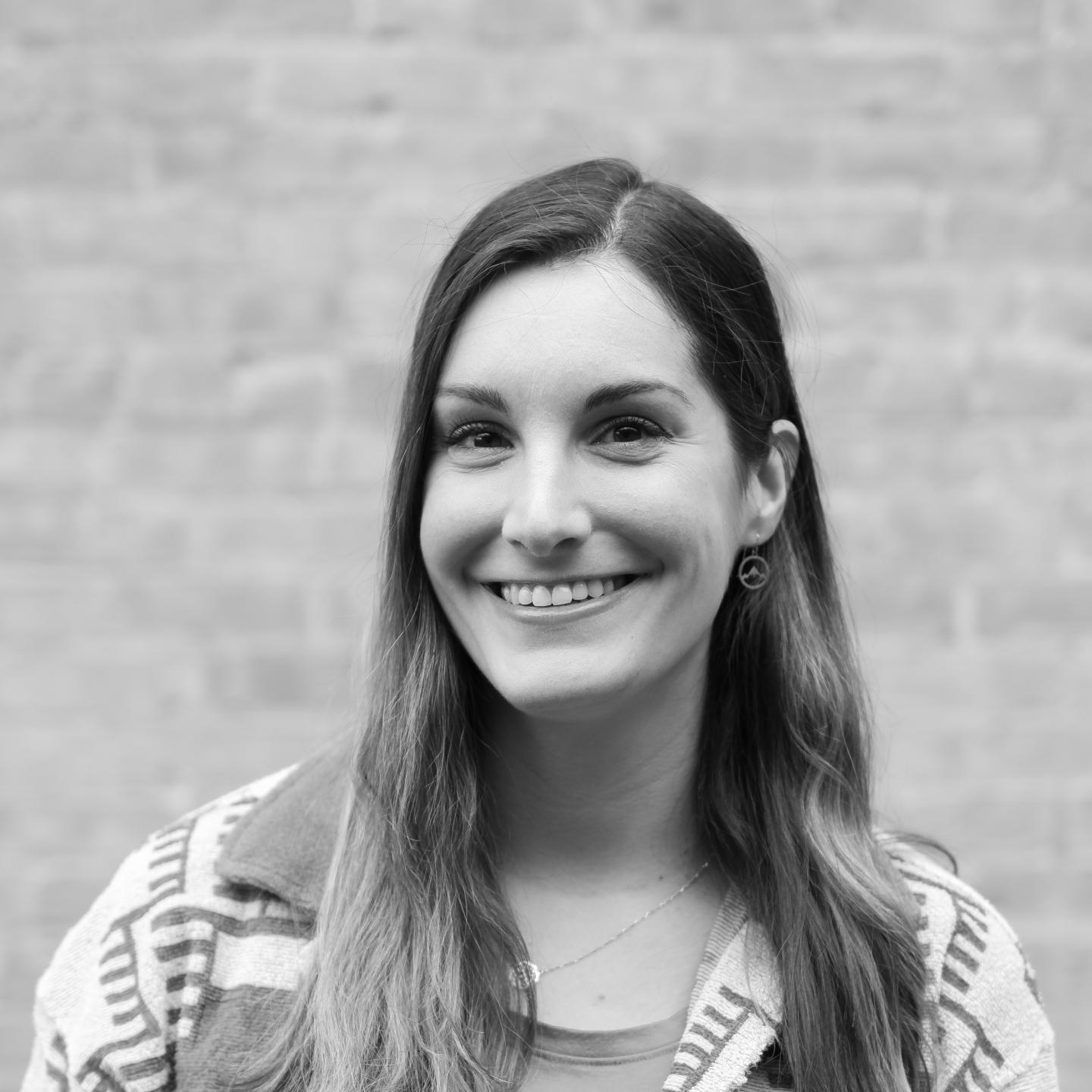 Smiling woman with long hair in front of a brick wall.