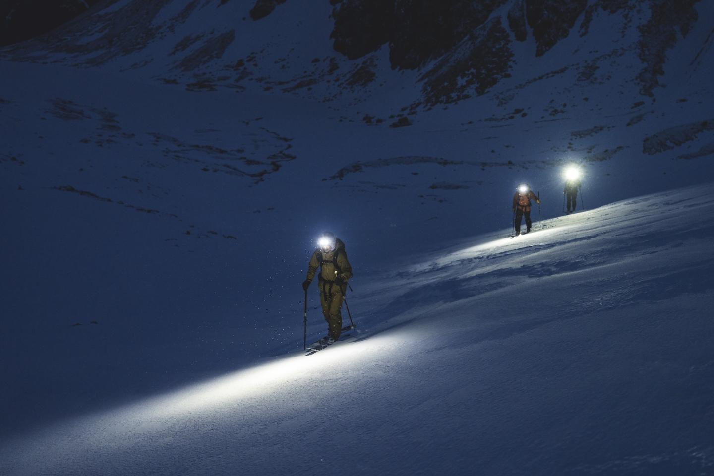 Two climbers with headlamps ascend a snowy slope at night.