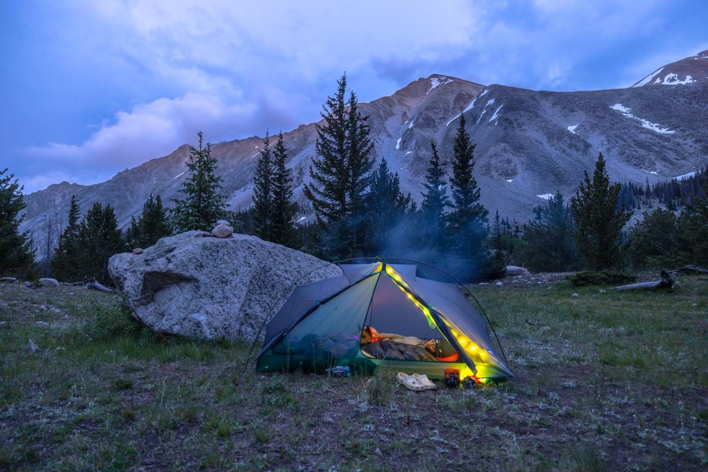 Tent glowing in a mountain meadow at dusk